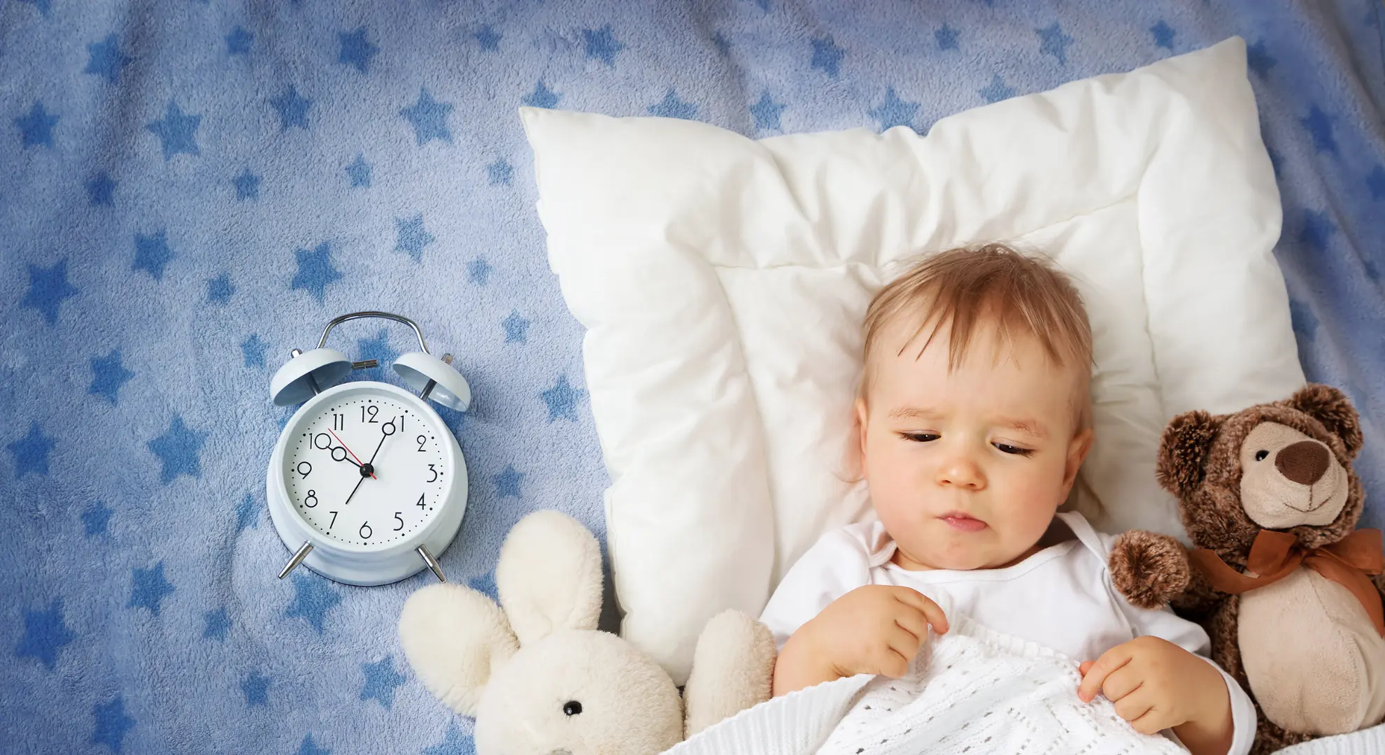 Changement d'heure d'été, bébé dans son lit avec horloge et doudous